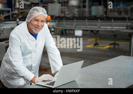 Portrait of happy male worker using laptop in factory Stock Photo