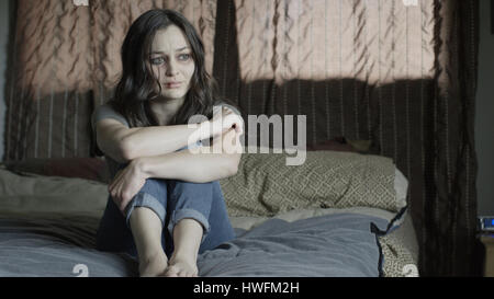Sad battered woman holding her knees and crying on bed Stock Photo