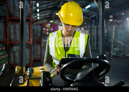 Female worker using digital tablet while sitting on forklift in warehouse Stock Photo