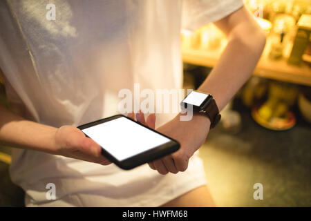 Mid-section of woman using smart watch while holding smartphone Stock Photo