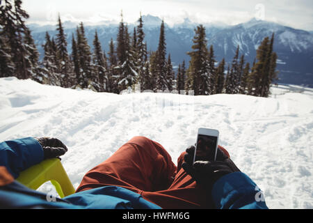 Low section of man holding mobile phone at snow covered mountain against trees Stock Photo