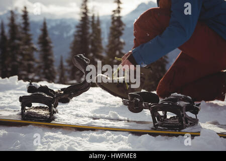 Low section of woman wearing shoe by snowboard at mountain during winter Stock Photo