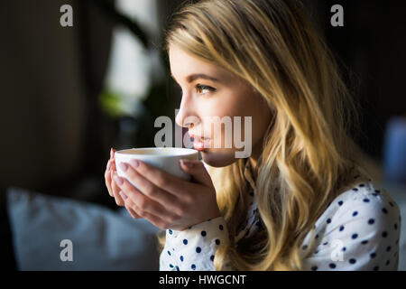 Portrait of young gorgeous female drinking tea and thoughtfully looking out of the coffee shop window while enjoying her leisure time alone, nice busi Stock Photo