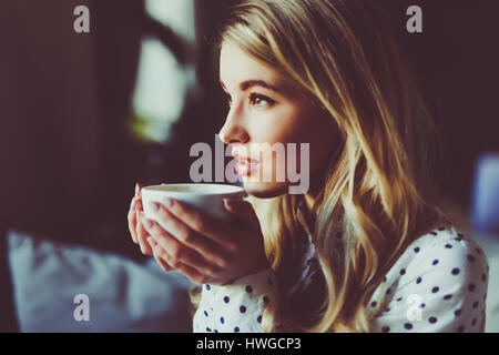 Portrait of young gorgeous female drinking tea and thoughtfully looking out of the coffee shop window while enjoying her leisure time alone, nice busi Stock Photo