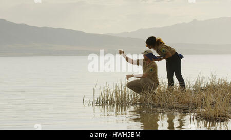 Profile of scientists working together and examining water sample in reeds at remote grassy lake shore Stock Photo