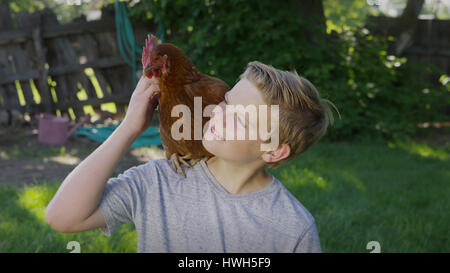 High angle view of smiling boy petting rooster on shoulder in backyard