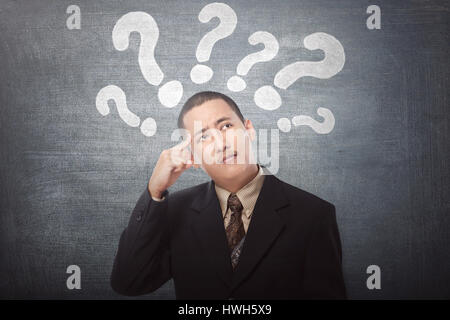 Young asian businessman confused with question marks above his head on black background Stock Photo