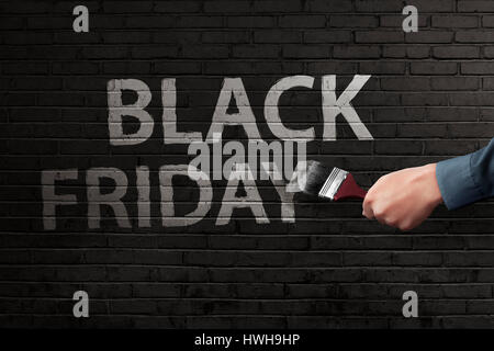 Man hand writing white Black Friday text with brush on the bricks wall Stock Photo