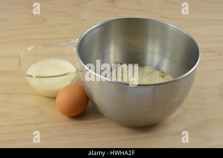 Ingredients for cornbread batter with mix in mixing bowl, egg and milk in measuring cup Stock Photo