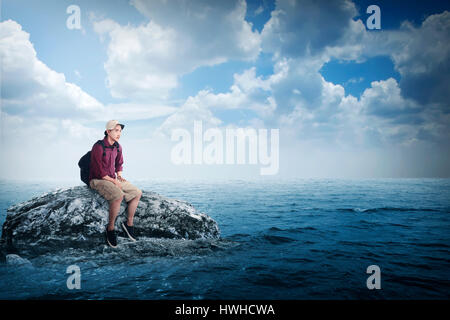 Young asian traveler sitting on the rock in the middle of the sea Stock Photo