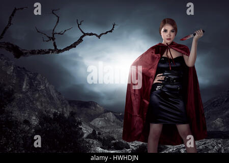 Beautiful asian witch woman holding bloody knife in the night, horror situation. Halloween concept image Stock Photo