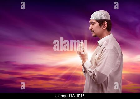 Young asian muslim man praying to god on silhouette background wearing cap Stock Photo