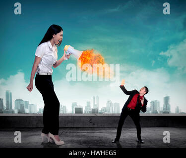 Big boss yelling to her employee with megaphone on fire. Work pressure concept Stock Photo