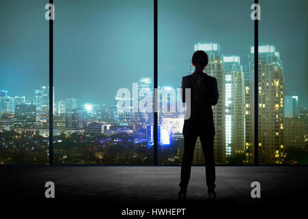 Woman standing in his office looking at the city at night. Business success concept Stock Photo