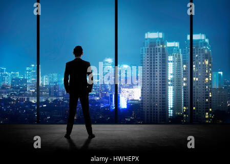 Man standing in his office looking at the city at night. Business success concept Stock Photo