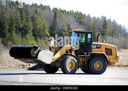 PAIMIO, FINLAND - MARCH 18, 2017: CAT 938K wheel loader and bucket sweeper at work to clean an asphalt yard at spring. Stock Photo