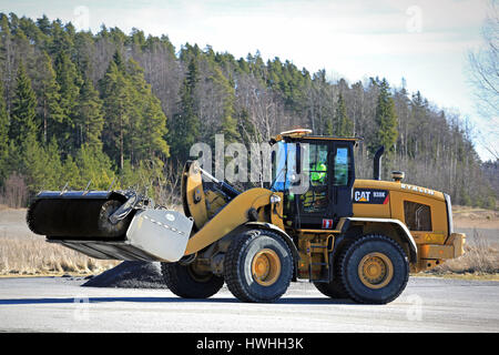 PAIMIO, FINLAND - MARCH 18, 2017: CAT 938K wheel loader and bucket sweeper at work to clean an asphalt yard at spring. Stock Photo