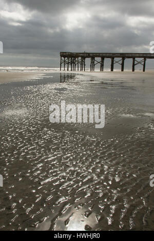Colorless scene of water in sand ripples with pier and heavy clouds in background Stock Photo