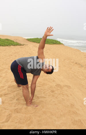 Man exercising on the beach, near the sea in trikonasana yoga pose Stock Photo