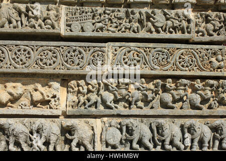 Detailed ornamented stone carving depicting Hindu mythology, foliage, horsemen and elephant procession on panels of shrine wall at Chennakesava Temple Stock Photo