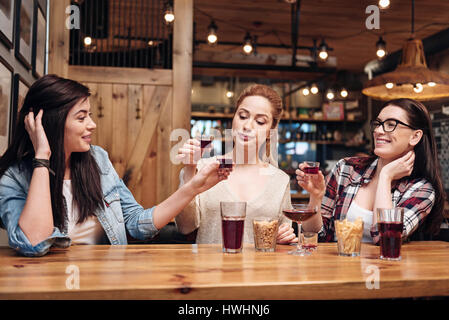 Drink something. Fastidious blonde pressing her lips sitting between her friends while drinking alcohol Stock Photo