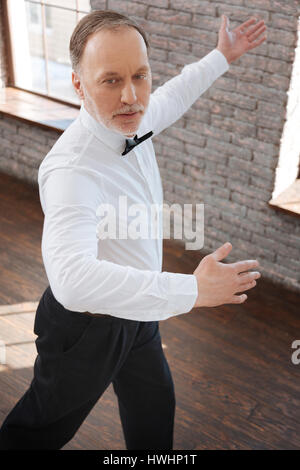 Enjoying classical art. Cheerful delighted flexible aging man performing in the ballroom while mastering dance skills and learning new dance step Stock Photo