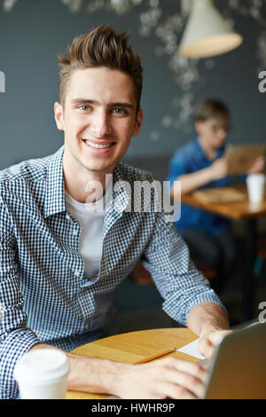 Portrait of handsome university student sitting in cyber cafe and working on his thesis, young woman with digital tablet and cup of coffee sitting beh Stock Photo