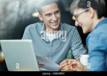 Portrait of cheerful university student holding paper in hands while helping his female course mate to study for difficult test in lovely coffeehouse Stock Photo