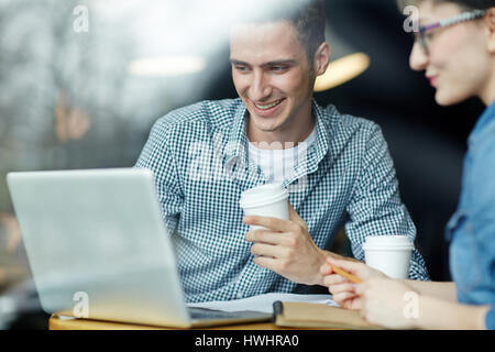 Waist-up portrait of smiling university students gathered together in cafe and doing homework, notebooks, papers, pencils and laptop located on table Stock Photo