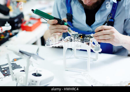 Closeup shot of unrecognizable man  testing electric current in circuit board of disassembled drone using multimeter tool on table in maintenance shop Stock Photo