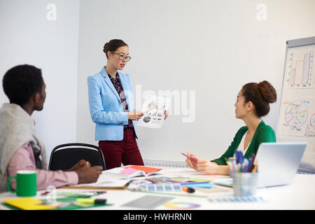 Young woman pointing at financial chart on paper while explaining data to colleagues Stock Photo