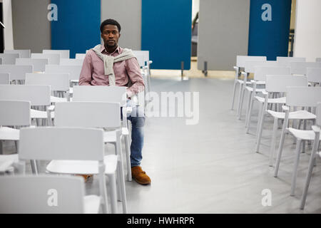 Serious student sitting on chair in empty conference-hall Stock Photo
