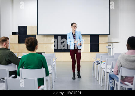 Happy young teacher talking to her students in conference-hall Stock Photo