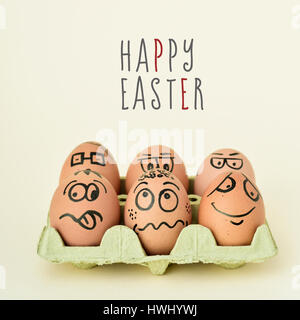 a pile of brown eggs ornamented with funny faces in a yellow egg carton, and the text happy easter on an off-white background Stock Photo