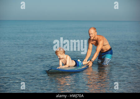 Athletic man with little boy teaching him surfing Stock Photo