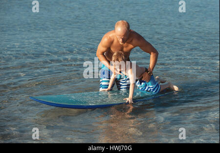 Athletic man with little boy teaching him surfing Stock Photo