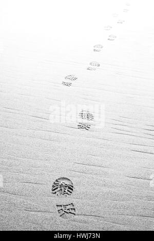 Footprints hiking boots on beach ,fading to white. Monochrome Stock Photo