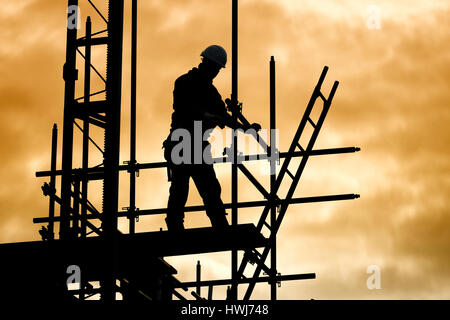 silhouette of construction worker against sky on scaffolding with ladder on building site at sunset Stock Photo