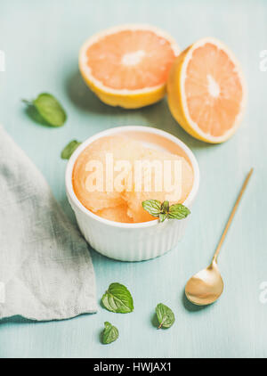 Pink grapefruit sorbet with fresh mint in white bowl over blue painted background, selective focus. Fresh healthy raw vegan summer dessert concept Stock Photo