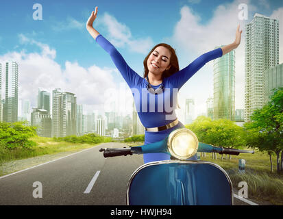 Beautiful asian woman riding a scooter while raise up both hands in the urban street background Stock Photo