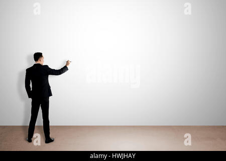 Business man writing something on empty white wall. You can put your message on the wall Stock Photo