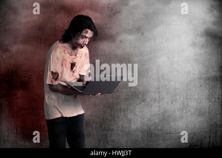Scary male zombie typing with laptop over grunge background Stock Photo