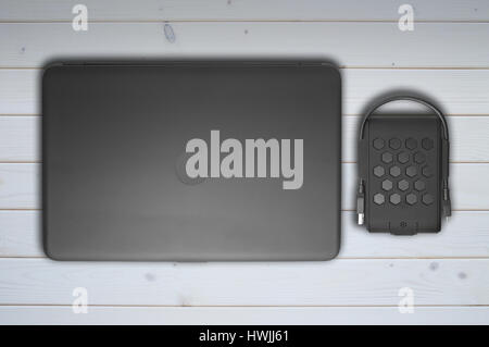 A closed laptop and an external hard drive lie on a light wooden background. View from above Stock Photo