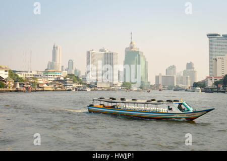 Bangkok, Thailand - February 18, 2017: Colorful boat approaches the pier while some of Bangkok skyline is seen on the background. Stock Photo