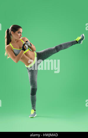 Athletic woman training her high kick in studio on green backgro