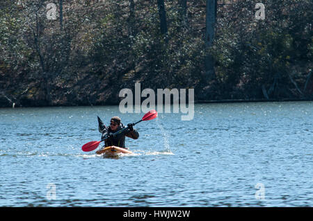 A SINGLE KYAKER PADDLES ACROSS A QUIET LAKE IN THE WINTER TIME. Stock Photo