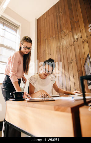 Vertical shot of two businesswoman working together on a new project. Female coworker going through some paperwork at their desk. Stock Photo