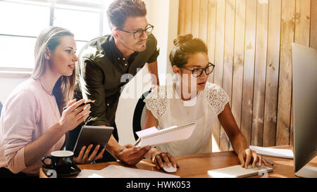 Shot of business team brainstorming while working on computer. Business people working together on project at startup office. Stock Photo