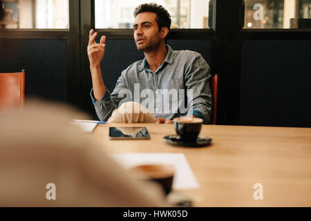 Shot of young man discussing with colleague in conference room. Businessman talking with coworkers in office.