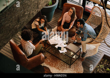 Top view of four business colleagues sitting on office lobby and discussing new ideas. Corporate business team meeting in office. Stock Photo